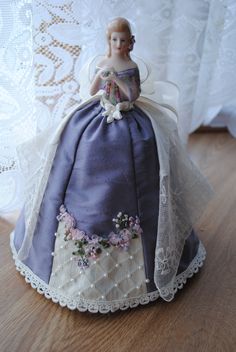 a doll sitting on top of a wooden table next to a white lace doily