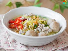 a white bowl filled with noodles and meatballs on top of a table next to napkins