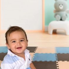 a little boy sitting on top of a rug in front of a teddy bear toy