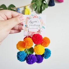 a hand holding a card with colorful pom poms hanging from it's side