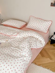 a bed with pink and white bedspread on top of wooden floor next to lamp