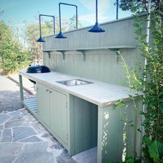 an outdoor kitchen is built into the side of a building with three lights hanging over it