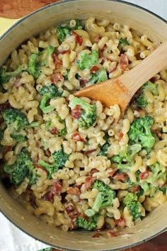 a wooden spoon in a pot filled with macaroni and broccoli