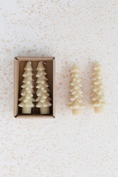 three small candles in a box on a table next to each other, one is white and the other is brown