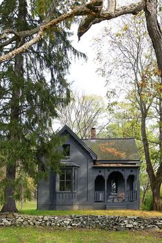 an old black house in the woods with trees around it and rocks on the ground