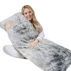 a woman is sitting on the floor holding a large gray furry animal blanket over her shoulder