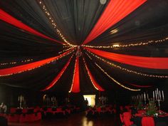 the inside of a tent decorated with red and black drapes, lights and tables