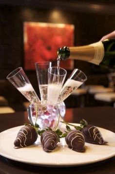 chocolate covered strawberries on a plate with champagne being poured into the glass and two wine glasses