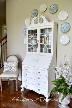 a white china cabinet sitting on top of a hard wood floor next to a chair