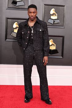 a man standing on top of a red carpet wearing black pants and a suit with sequins