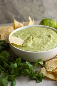 a white bowl filled with guacamole surrounded by tortilla chips