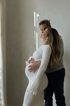 a man and woman standing next to each other in front of a window with their hands on the belly