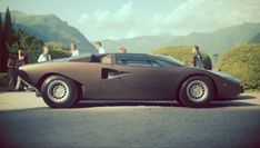 a brown sports car parked in front of some people