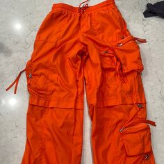 Baggy Parachute Pants With Side Panel Pockets. Adjustable Ruched Gathered Drawstring Hem. 100% Polyester. Size Xs Color Is Orange. Worn Twice Excellent Condition Utility Style Parachute Pants For Summer Streetwear, Summer Utility Parachute Pants For Streetwear, Summer Streetwear Parachute Pants With Multiple Pockets, Summer Streetwear Parachute Pants With Side Pockets, Summer Techwear Parachute Pants With Cargo Pockets, Summer Nylon Parachute Pants With Functional Drawstring, Summer Nylon Parachute Pants With Drawstring, Summer Streetwear Cargo Pants With Drawstring, Summer Nylon Parachute Pants With Pockets