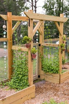 an outdoor garden with plants growing on the sides and hanging from wooden posts, in front of a fence