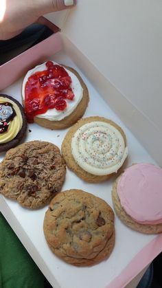 a person holding a box full of cookies and pastries with frosting on them