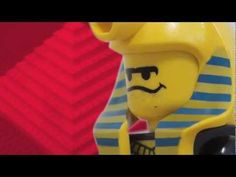 a lego man with a yellow hat and blue striped shirt is holding a black object