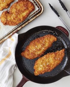 two fried fish fillets in a frying pan next to a spatula and tongs