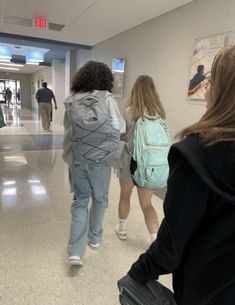 several people walking down a hallway in an airport with luggage on the ground and one person carrying a backpack