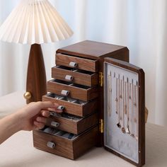 a wooden jewelry box is open and showing the contents in its storage compartment, with a hand reaching for it