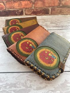 three leather wallets with embroidered designs on them sitting on a wooden table next to a brick wall