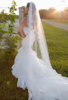 a woman in a wedding dress standing next to a tree with her veil pulled back