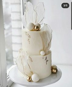 a three tiered cake with white frosting and gold decorations on it's side