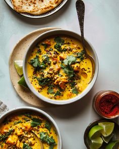 two bowls filled with soup next to some pita bread and lime wedges on the side