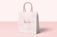 a white shopping bag with pink handles on a pink background that says sucre phys biscuit