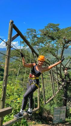 a woman is zipping through the air on a rope bridge with trees in the background