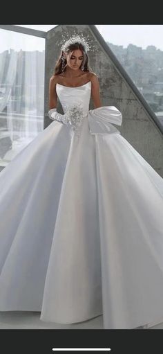 a woman in a white wedding dress standing by a window with her hands on her hips