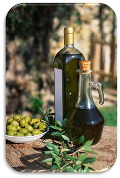 an olive oil bottle next to a bowl of green olives on a tree stump