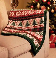 a couch with a christmas blanket on it next to a christmas tree