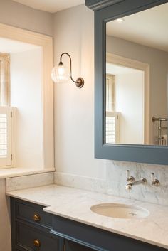 a bathroom vanity with marble counter top and blue cabinetry, along with a large mirror over the sink