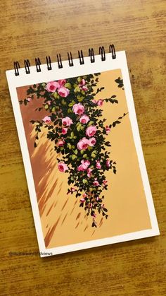 a spiral notebook with pink flowers on it sitting on top of a wooden table next to a pen