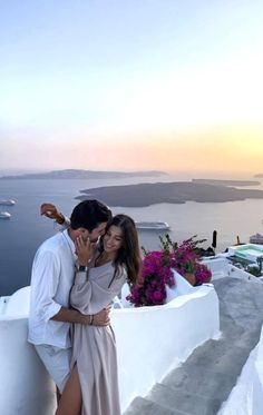 a man and woman standing next to each other in front of the ocean at sunset