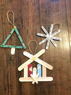 three popsicle christmas tree ornaments on a wooden table with snowflakes hanging from them