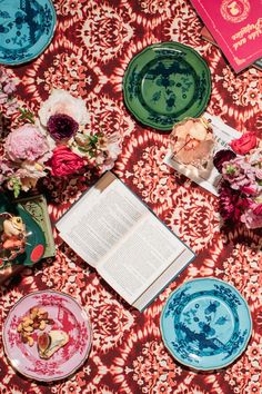 an open book on a table with plates and flowers