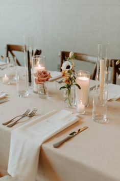 the table is set with white linens, silverware and candles for an elegant dinner