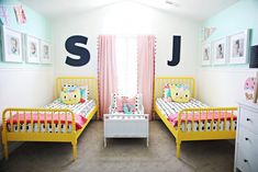 two yellow beds in a room with pink curtains and pictures on the wall above them