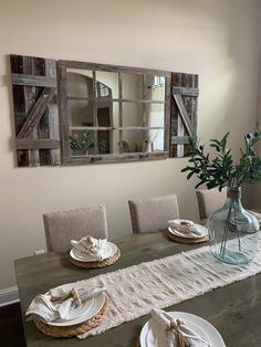 a dining room table with plates and place settings on it, along with a vase filled with flowers