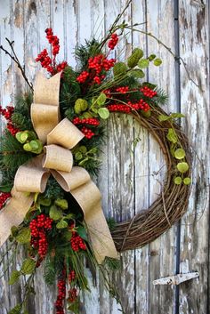 a wreath with red berries and greenery on it is hung on a wooden fence