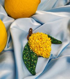 a yellow and green brooch sitting on top of a blue cloth next to two lemons