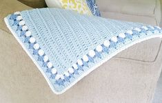 a blue and white crocheted afghan sits on a beige couch next to pillows