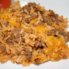 a white plate topped with rice covered in ground beef and cheesy sauce next to a tomato