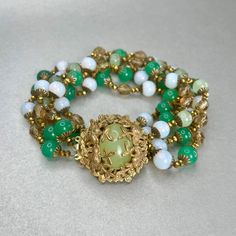 "Vintage Miriam Haskell Green Bracelet, Gold tone Multi Strand Jade Glass Bead Bracelet, Midcentury Collectible Signed Jewelry, Gift for Her. Era: Around 1950- 1951. Designer Signed: Miriam Haskell. Measurements: - Length Around Wrist : 8 1/2\" - Width: 1 1/2\" Details: -Metal Color: Gold - Embellishments: Gold Tone Plating, Pendant with Light Green Glass Stone in the middle. Five gleaming Strands of small Round Beads that are linked in-between by tiny Gold beads strands. Glass Beads: imitation Elegant Round Spacer Beads, Vintage Adjustable Green Beaded Bracelets, Formal Vintage Beaded Bracelets With Round Beads, Elegant Multi-strand Polished Beaded Bracelets, Vintage Beaded Bracelets For Formal Occasions, Vintage Green Jubilee Bracelet, Vintage Gold Beaded Bracelet With Spacer Beads, Adjustable Vintage Jewelry With Spacer Beads, Vintage Adjustable Beaded Bracelets With Spacer Beads