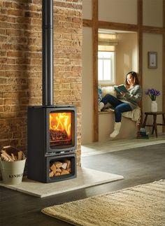 a woman sitting on a couch reading a book in front of a wood burning stove