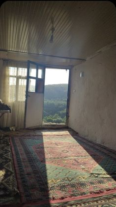 a room with a large rug on the floor next to a window and door that leads out onto a valley