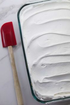 a red spatula sitting on top of a pan filled with white frosted cake