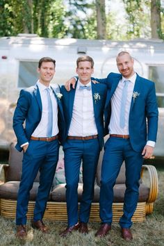 three men in blue suits standing next to an airstream with their arms around each other